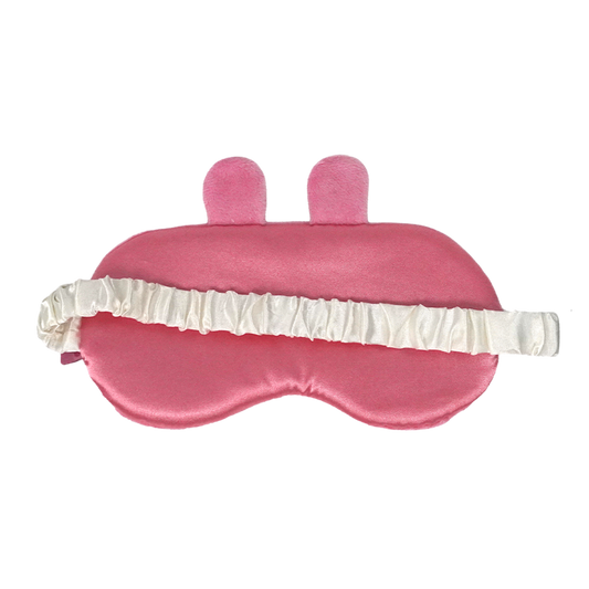 A pink satin sleep mask with two small upright bunny ears on top and a white ruffled elastic strap, shown on a plain white background.